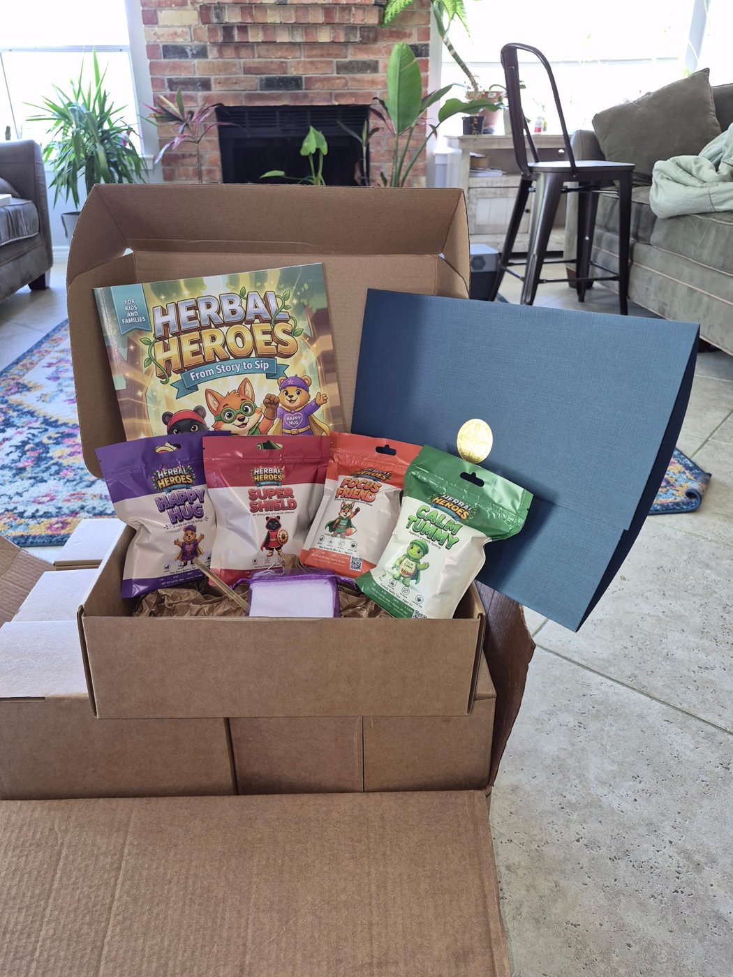 The Herbal Heroes First Edition Founders Bundle in an open shipping box with book, four tea pouches and navy folio with gold seal